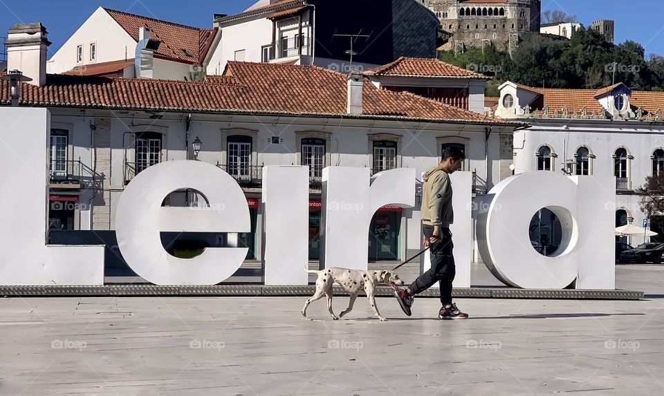 A man walking a Dalmatian dog, past large white letters the read Leiria