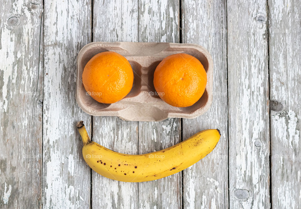 Three fruits on old wooden table. One banana and two oranges. Fun shape of smile.