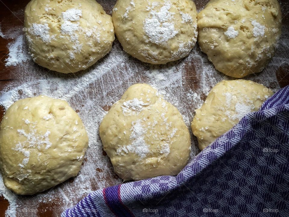 Fresh yeast dough formed into balls lies on a wooden board dusted with flour
