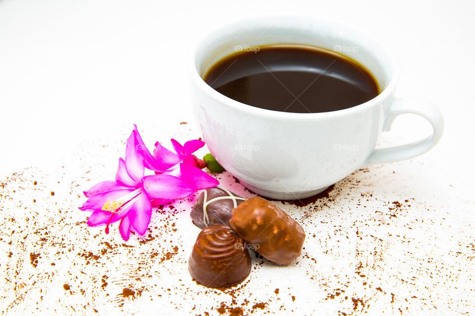 Close up of three milk chocolates and coffee with a flower and cocoa sprinkled.