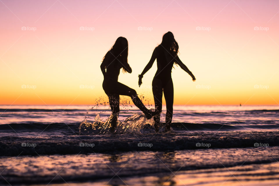 Women dancing in the ocean during a colorful sunset by the beach in summer
