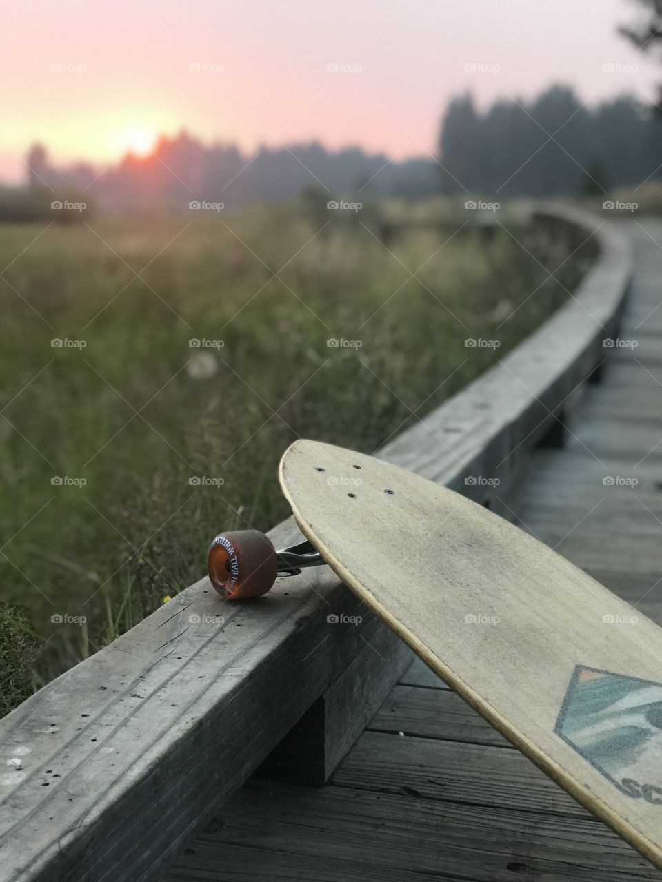 Hanging up the skateboard to stop and view the red sun set behind the tree line. 