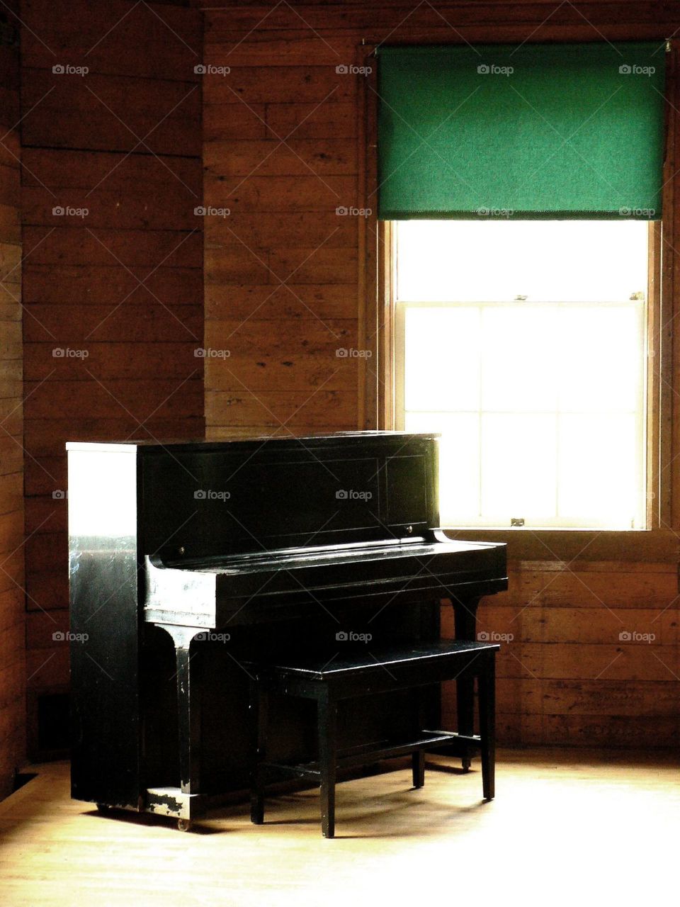Black piano . A single upright piano stands alone against a green shaded window
