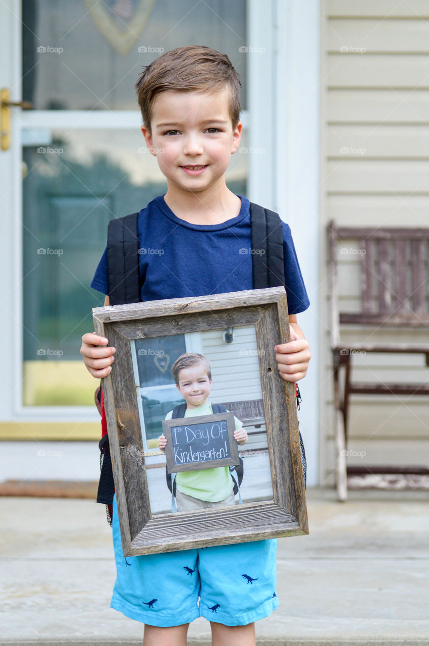 Young boy holding a picture outdoors on his first day of school