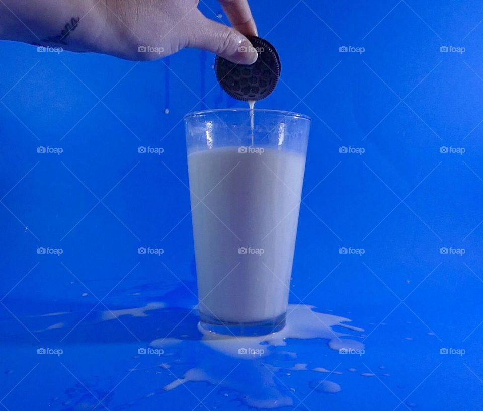 A cookie dunking into a cup of milk with a blue background