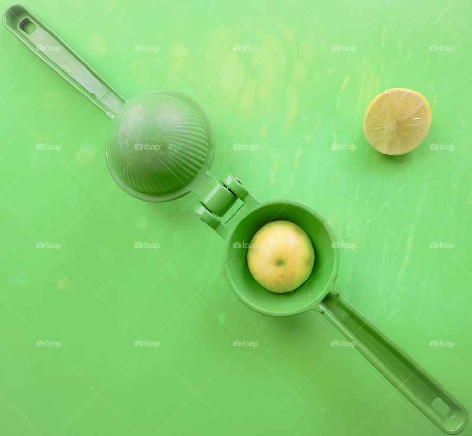 Round yellow ripe key lime half in a manual circular citrus squeezing utensil.  The utensil is placed open and diagonally on a matching green and yellow surface.