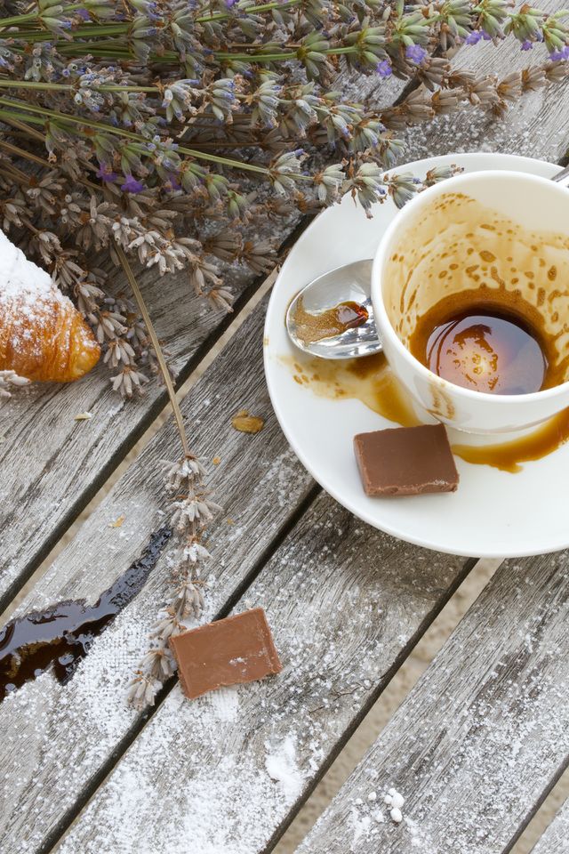Empty coffee cup, pieces of milk chocolate, sugar powder, croissant on a wooden surface. High angle shot.