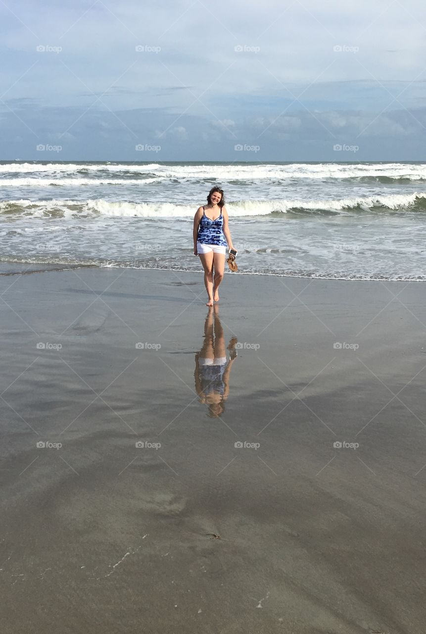 Woman walking at beach holding mobile phone and footwear in hand