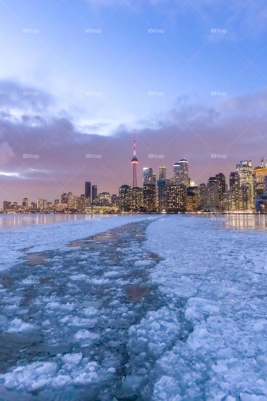 A ferry making its way across a frozen icy lake during a polar vortex with a colorful blue hour sky just after sunset. The Toronto skyline in the background 