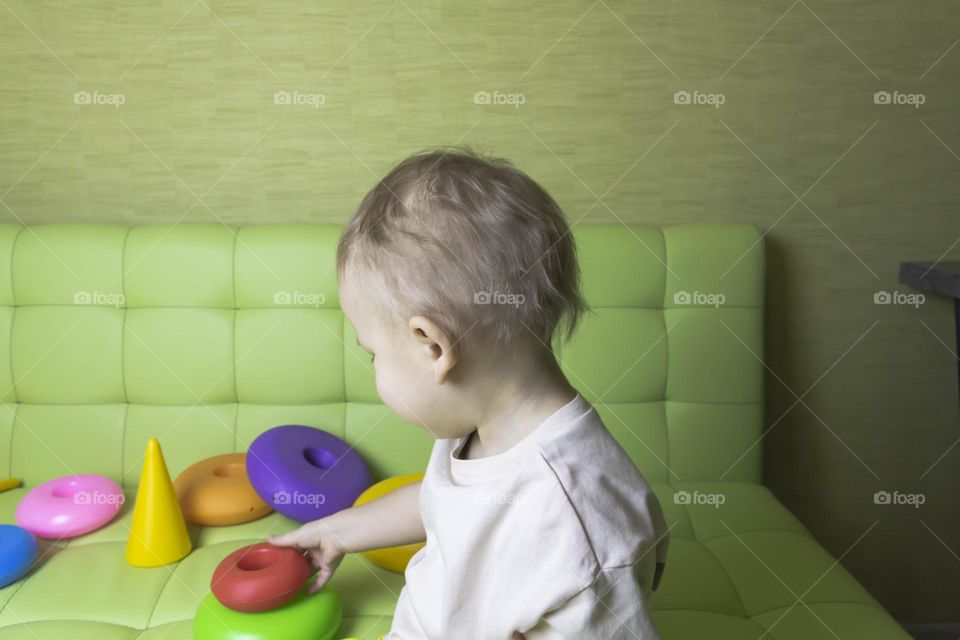 The child is having fun playing a bright pyramid educational toy, sitting on a green sofa.