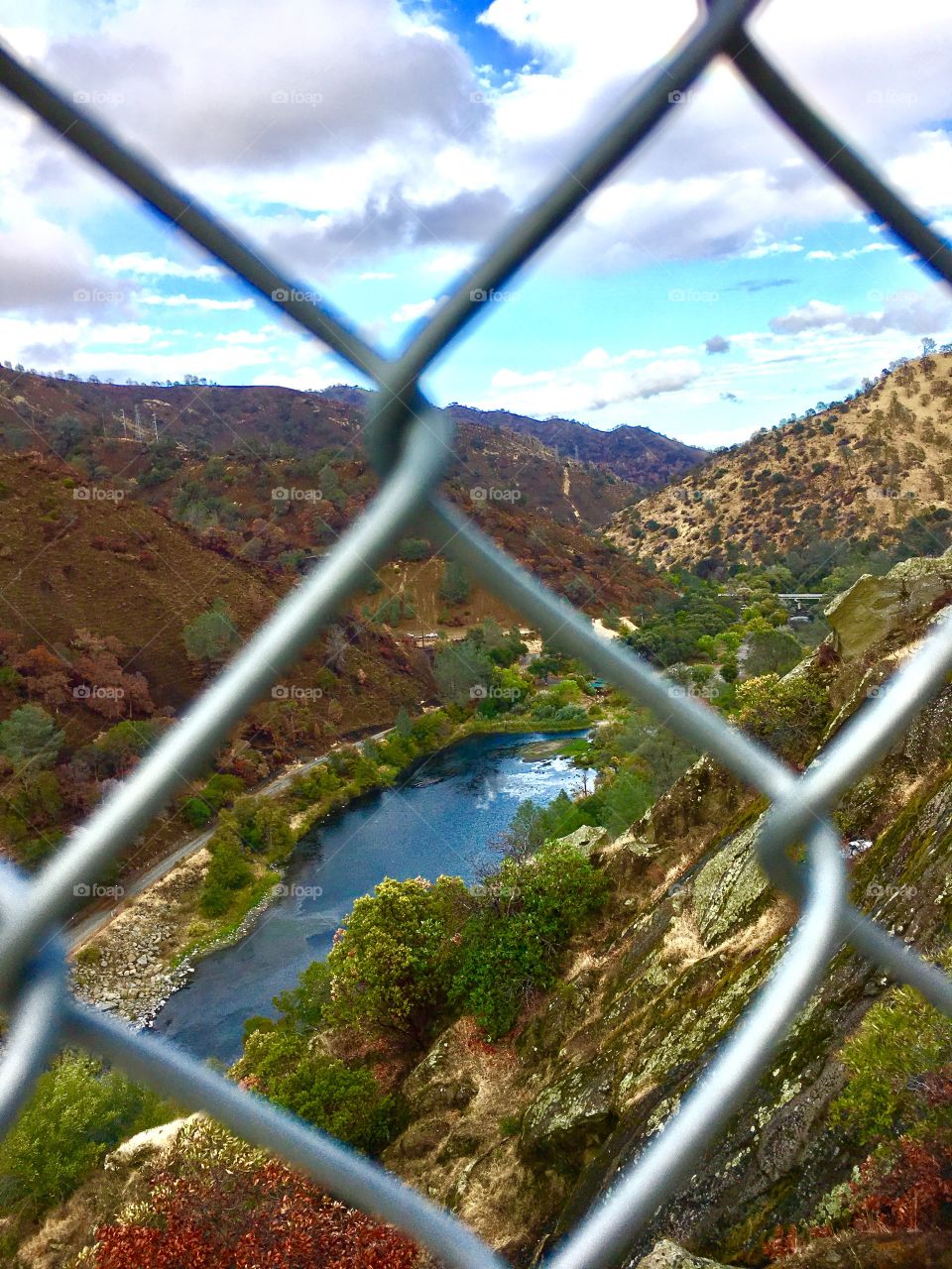 Scenic view of lake and mountains through chain linked fence. 