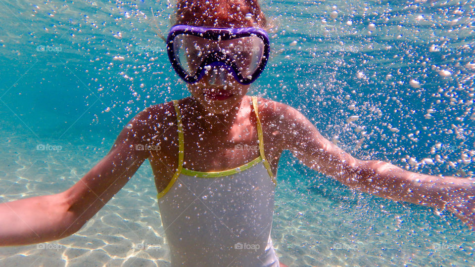 young girl diving underwater with googles in white swimsuite