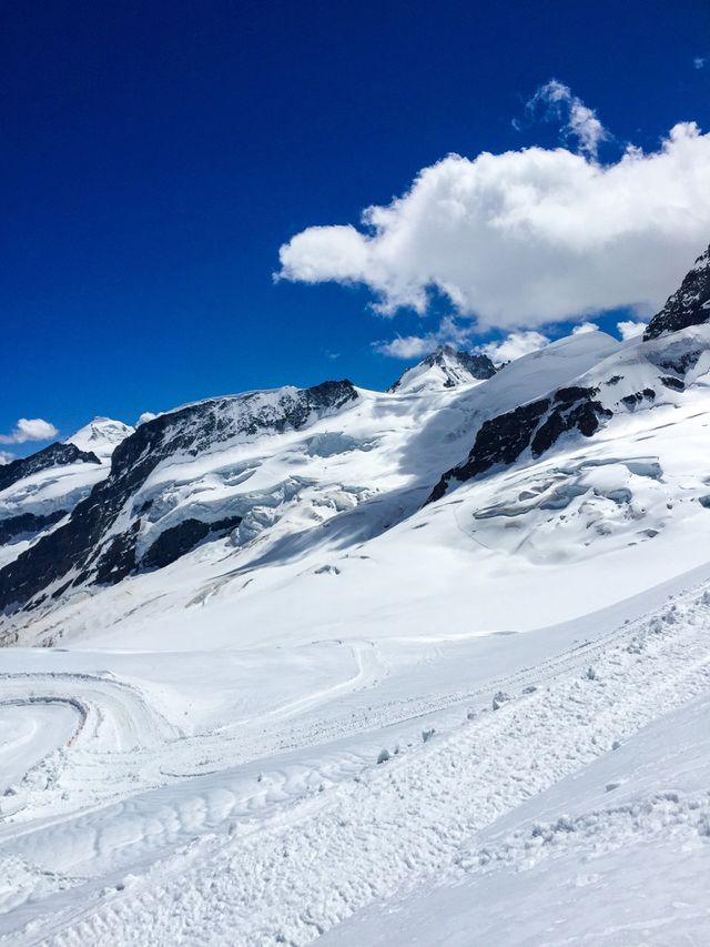 There is a lot of white snow on the top of the mountain , dark blue sky and big white cloud, day has many sunny but at here is very cold
