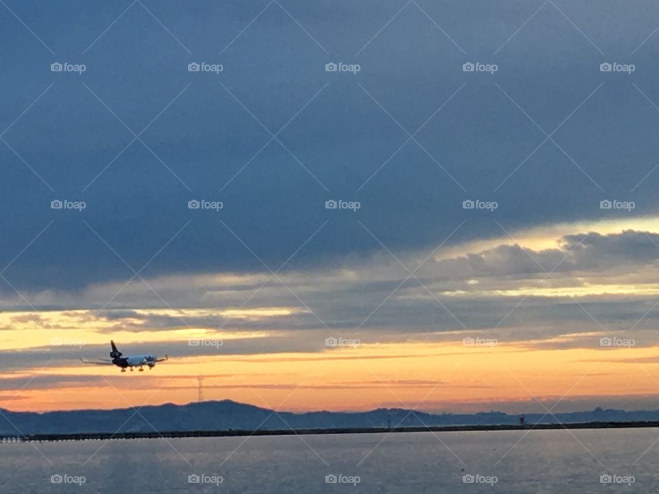 Plane landing at Oakland international airport with the sunset by the ocean in the backdrop 