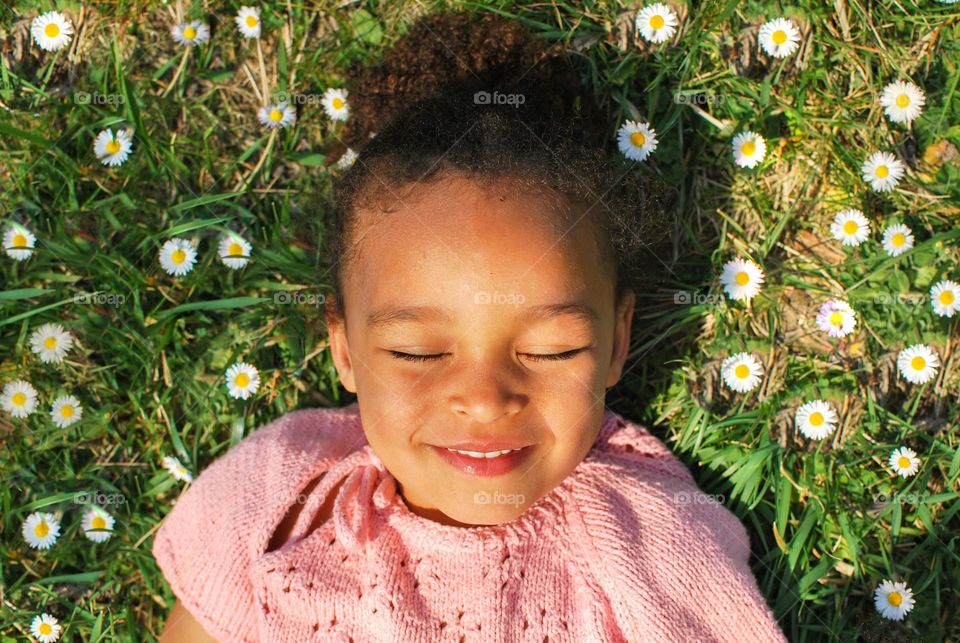 Little girl lying in a field of daisies, smiling and enjoying the sun