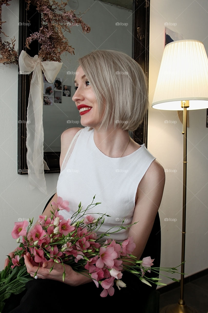 Beautiful woman with red lipstick is smiling and holding pink flowers 