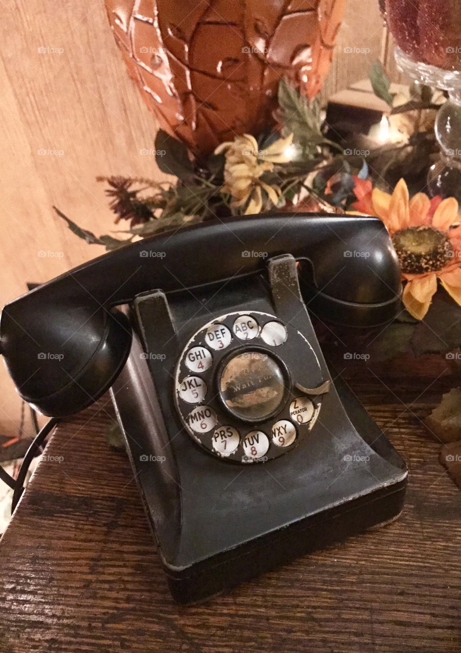Old black rotary style phone on a desk with autumn flowers by it, close up shot
