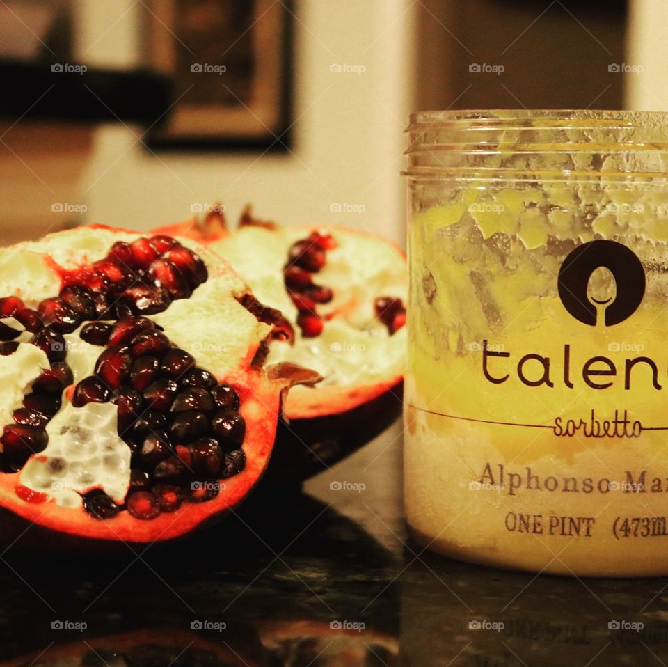 Half-filled pint of Alphonso Mango-flavored Talenti Sorbetto  next to halved pomegranate