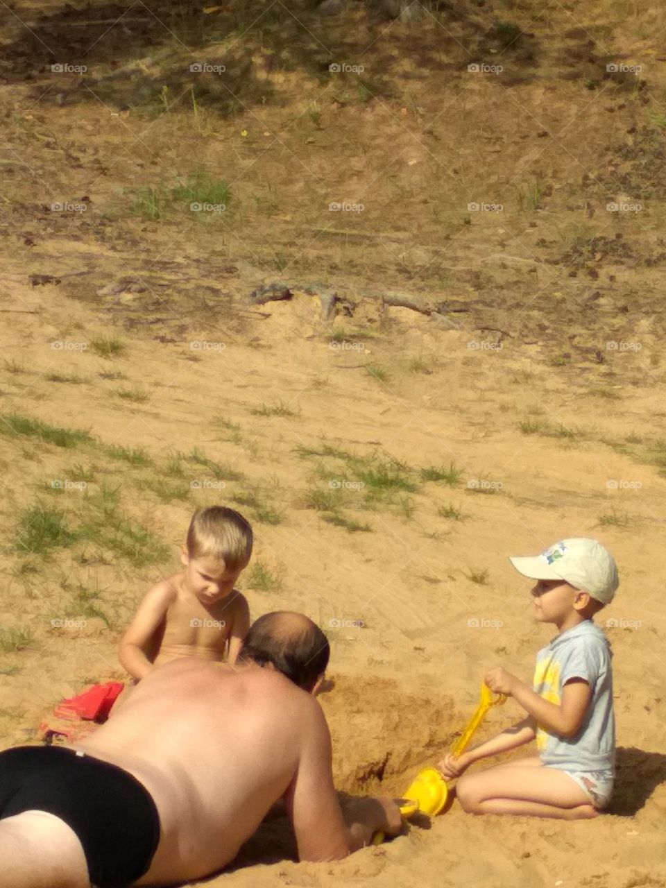 grandpa lies on the sand playing with children on the lake shore