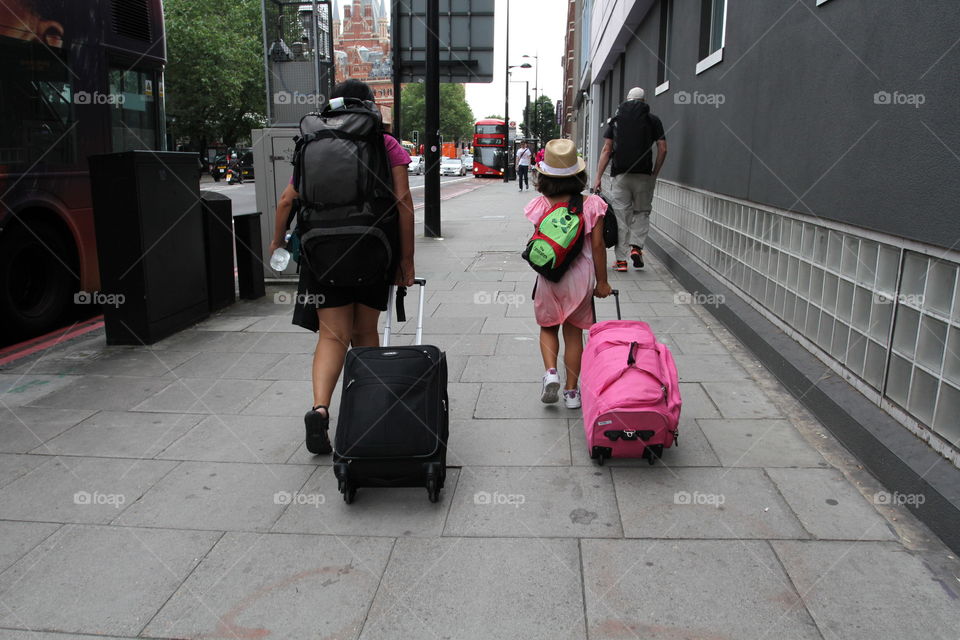 A mother and daughter pulling their suitcases behind them on their way to a train station in the city of London 