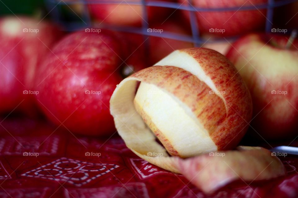 Fruits - Gala apples in a wire basket with a partially peeled apple and peeler on a red bandana-print tablecloth