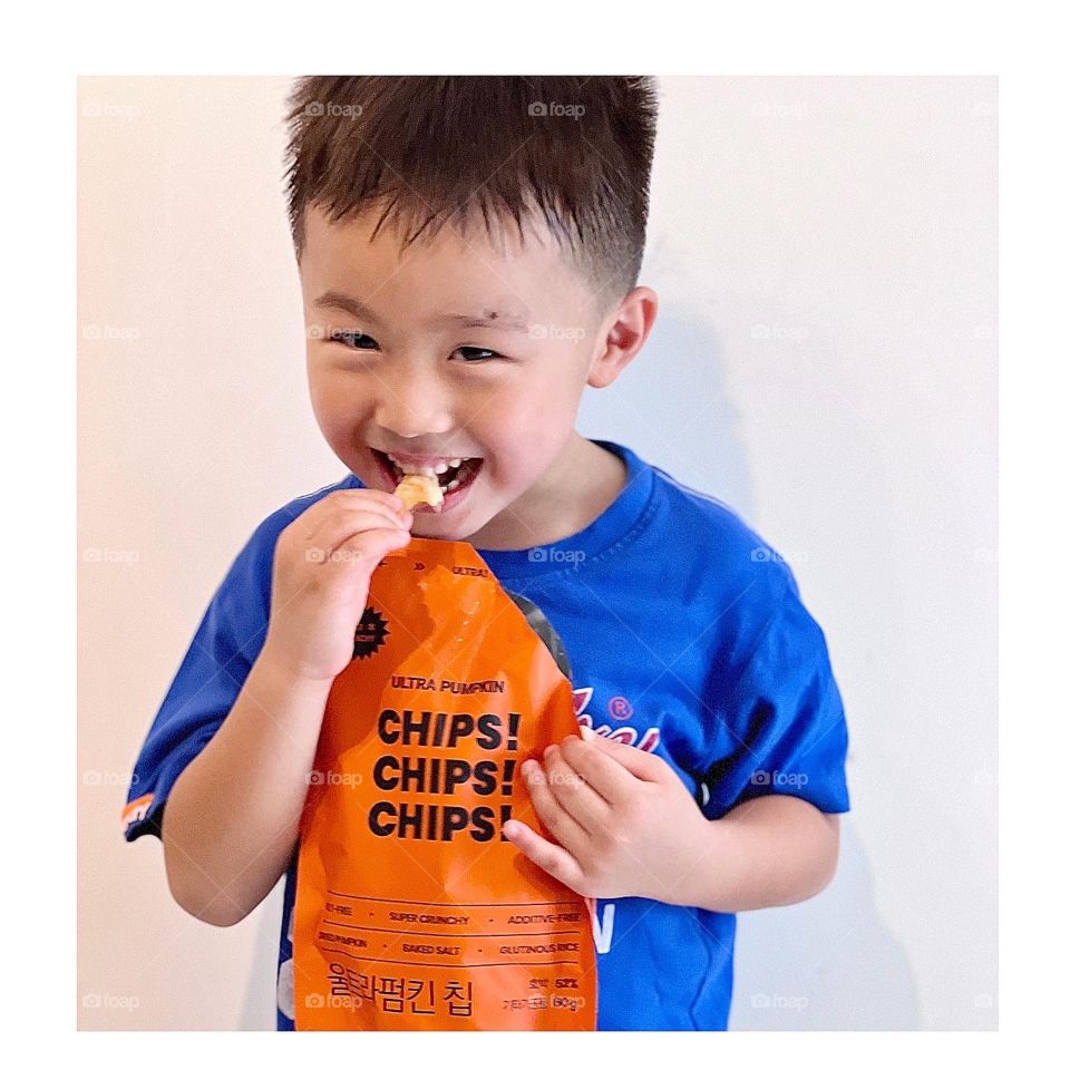 Asian boy eating Halloween trick or treat snacks made of pumpkin chips