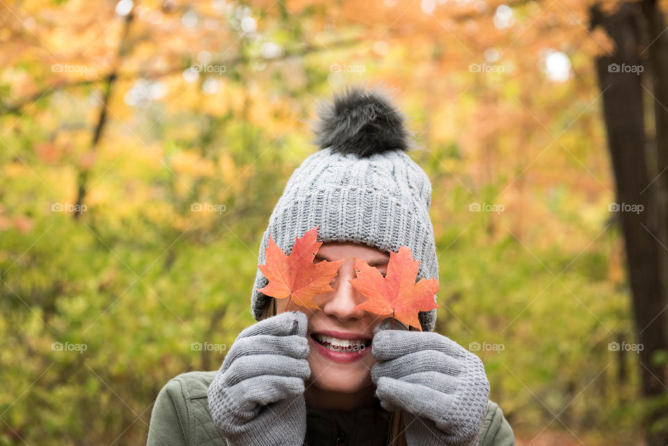 Young woman smiling and playfully holding a leaf over each eye outdoors during the fall 
