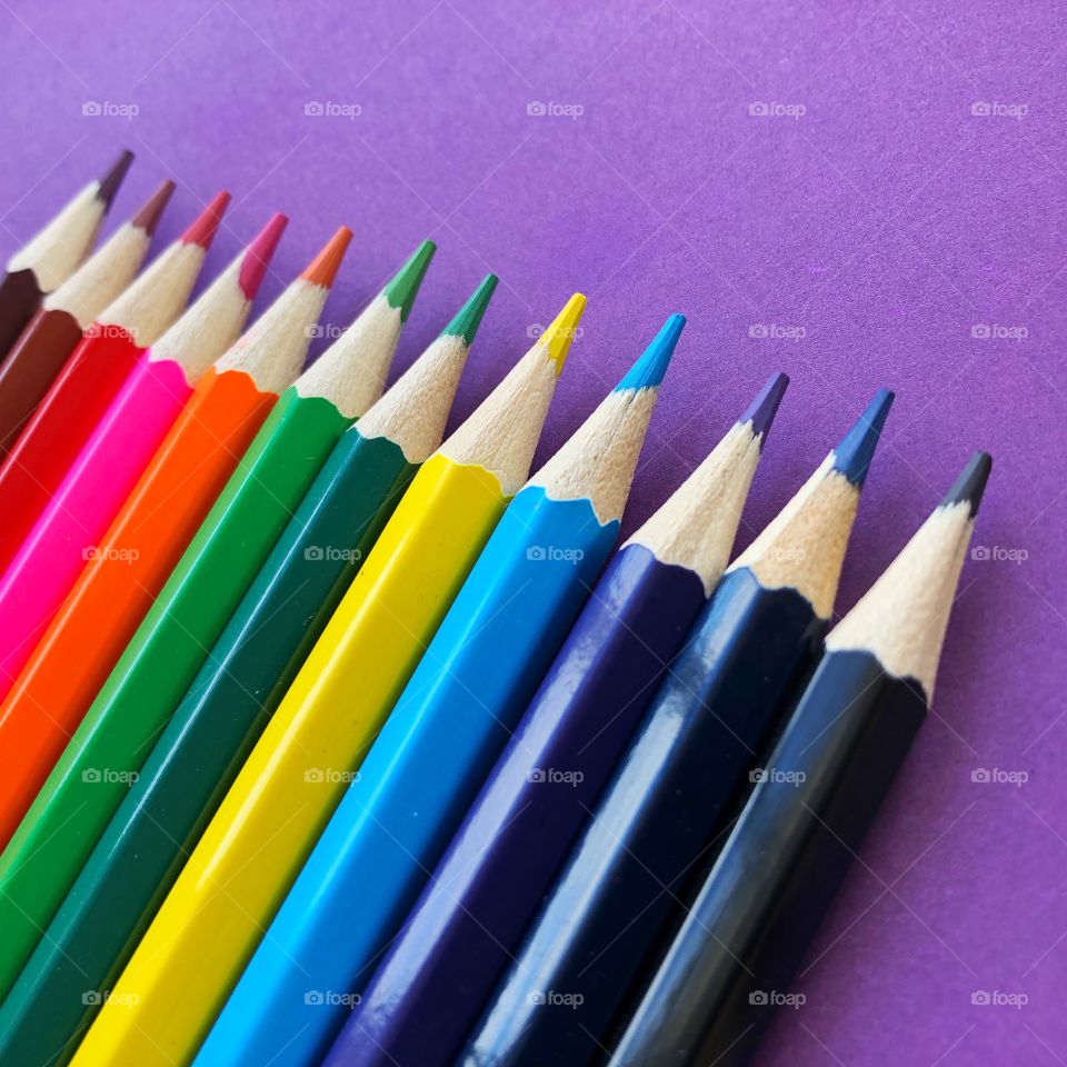 Rainbow multicoloured sharp pencils in a row on a purple background 