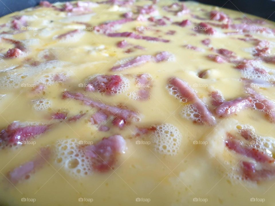 a close up portrait of bacon and eggs frying in a frying pan almost ready to be eaten.