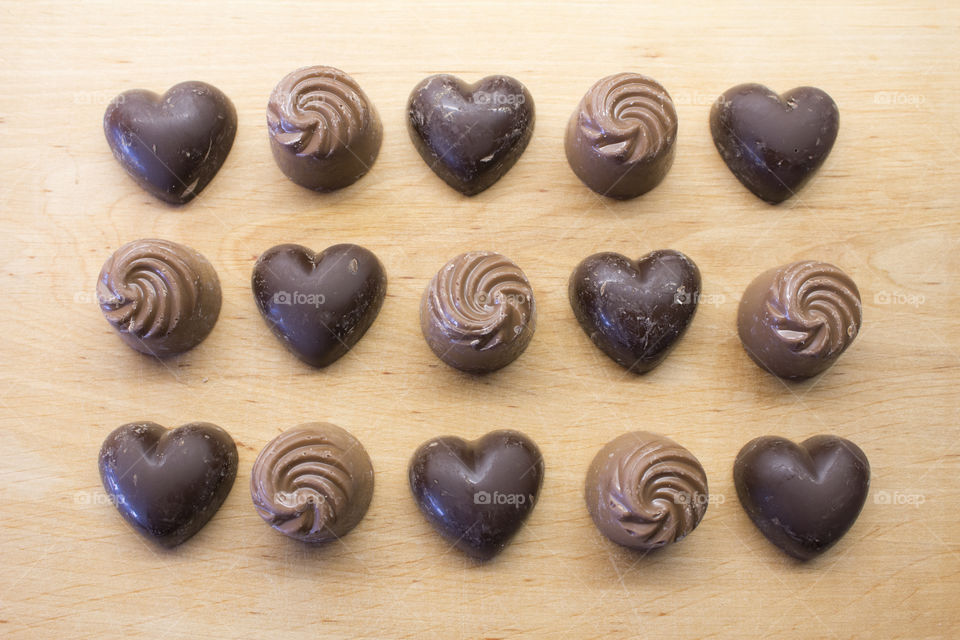 Dark chocolate hearts and milk chocolate swirls in rows on wood 