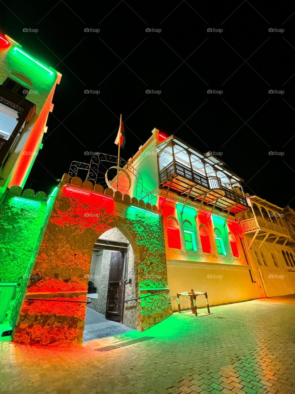 A traditional Omani house lit up with the Oman flag colours red, white and green.