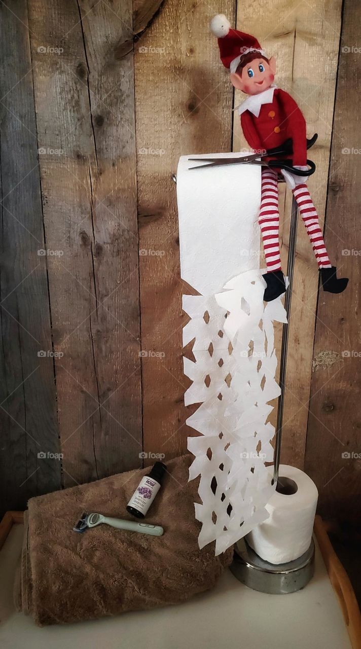 Elf on the shelf making toilet paper snowflakes.
