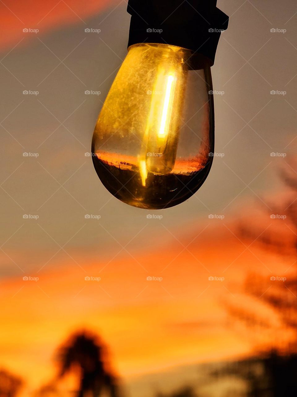 A brilliant orange sunset is reflected in a outdoor light fixture and is visible in the background