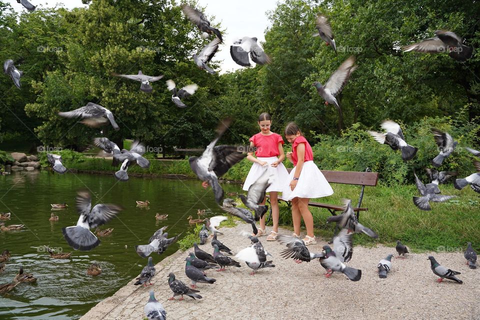 Two girls feeding pigeons in the city park