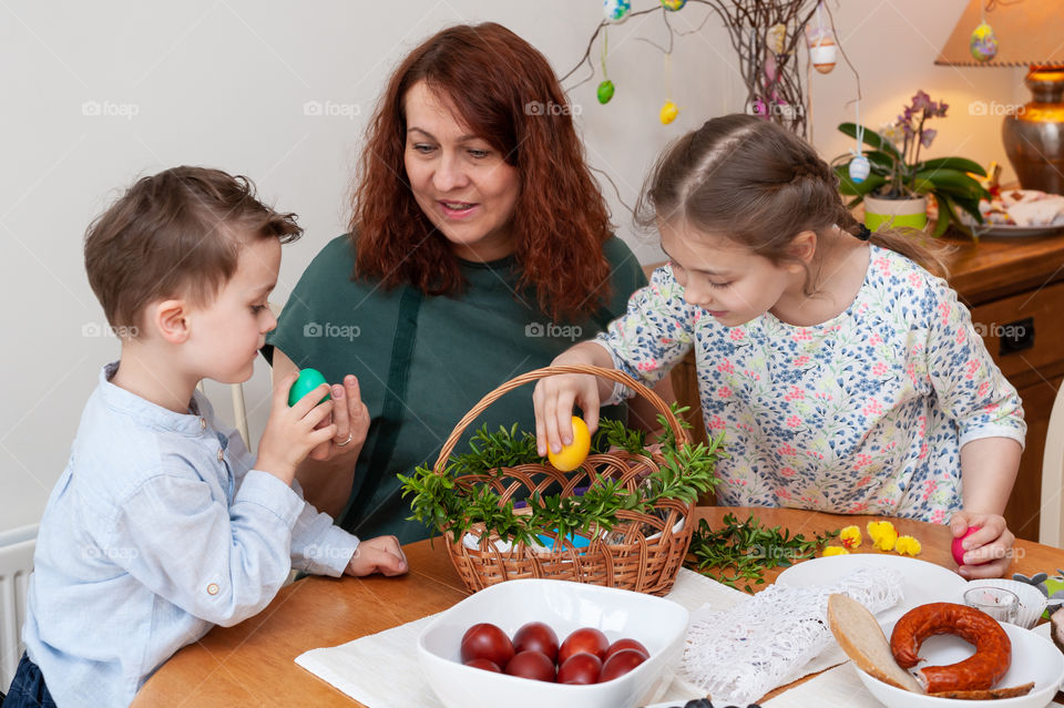 Mother and children preparing traditional Easter basket with food ingredients.