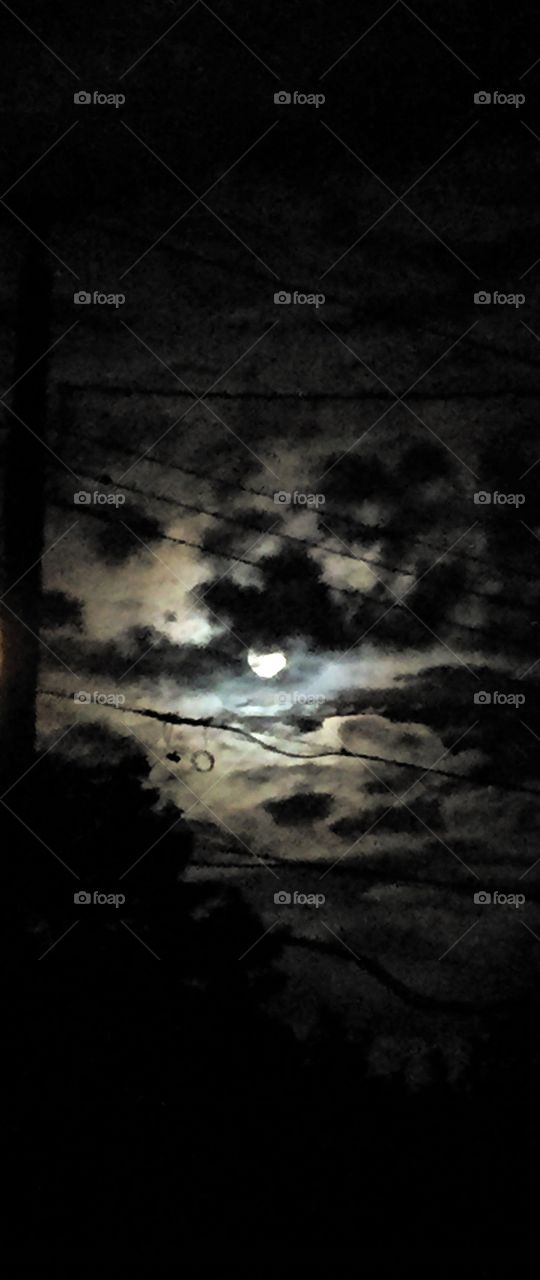 A full moon ensconced in clouds and wires.