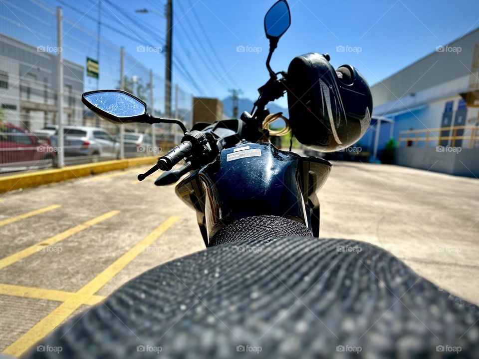 Close up of black motorcycle parked in a parking lot with a helmet hanging on it, in a sunny day.