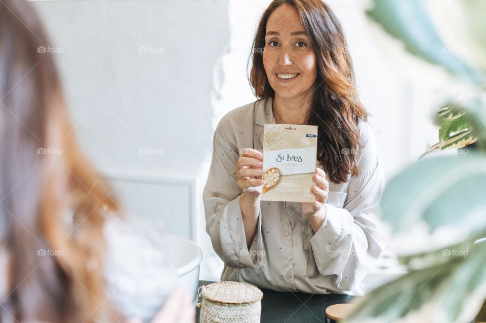 Woman with long hair with sheet mask st. ives in hands in bathroom at home 