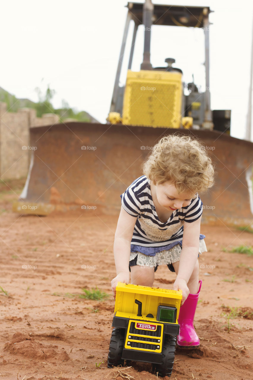 Little girl playing with toy vehicle in front of bulldozer