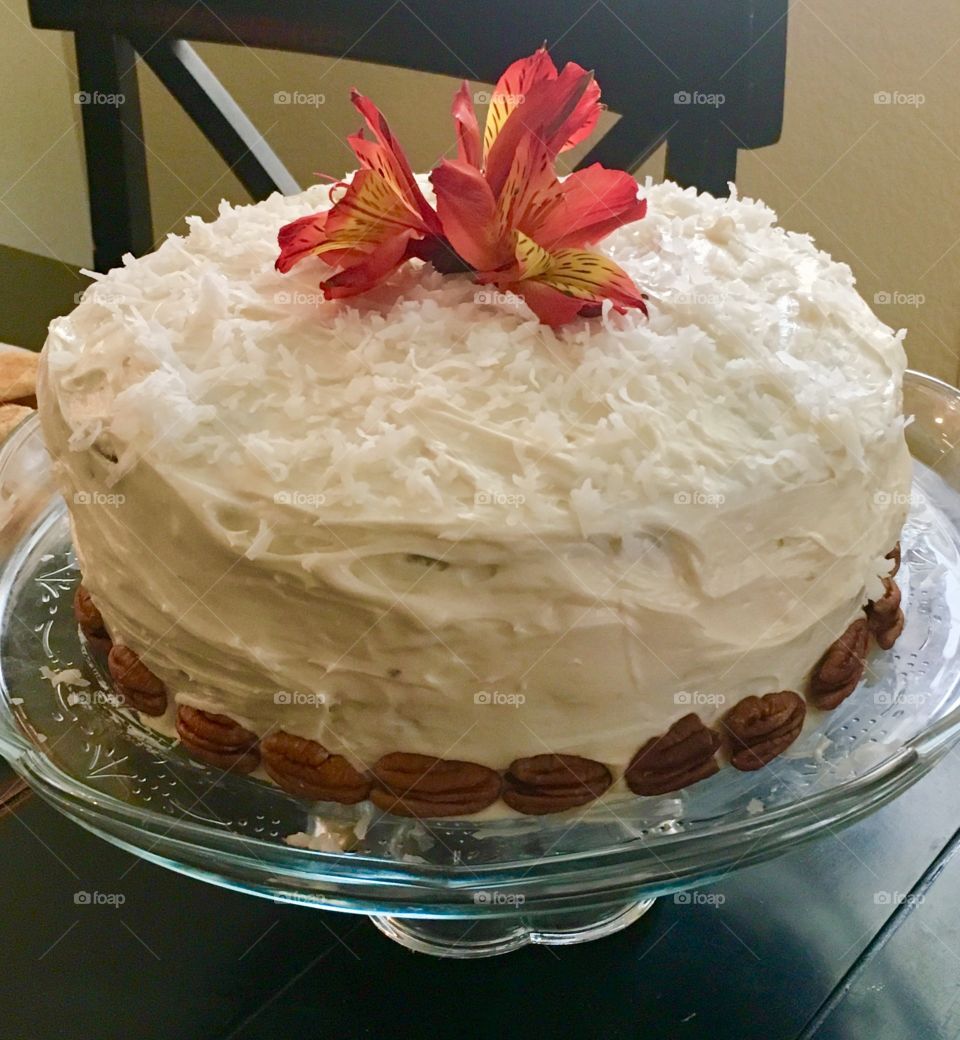 Homemade white cake with pecans and coconut frosting and a red fresh flower on top.