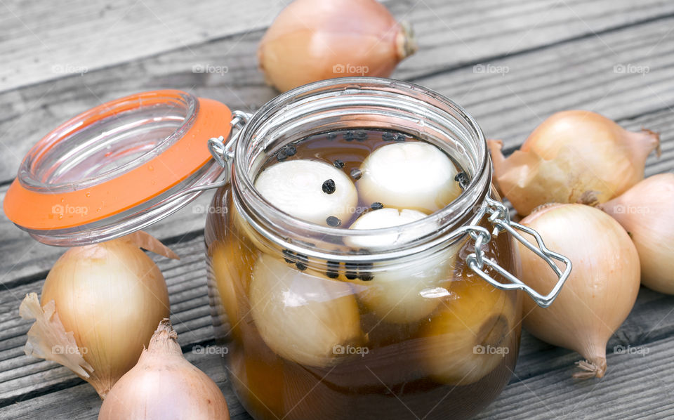Closeup view if an open pickled onion jar on a wooden table.