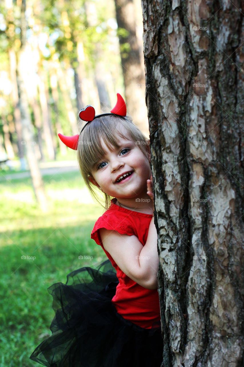 Adorable girl standing behind tree trunk