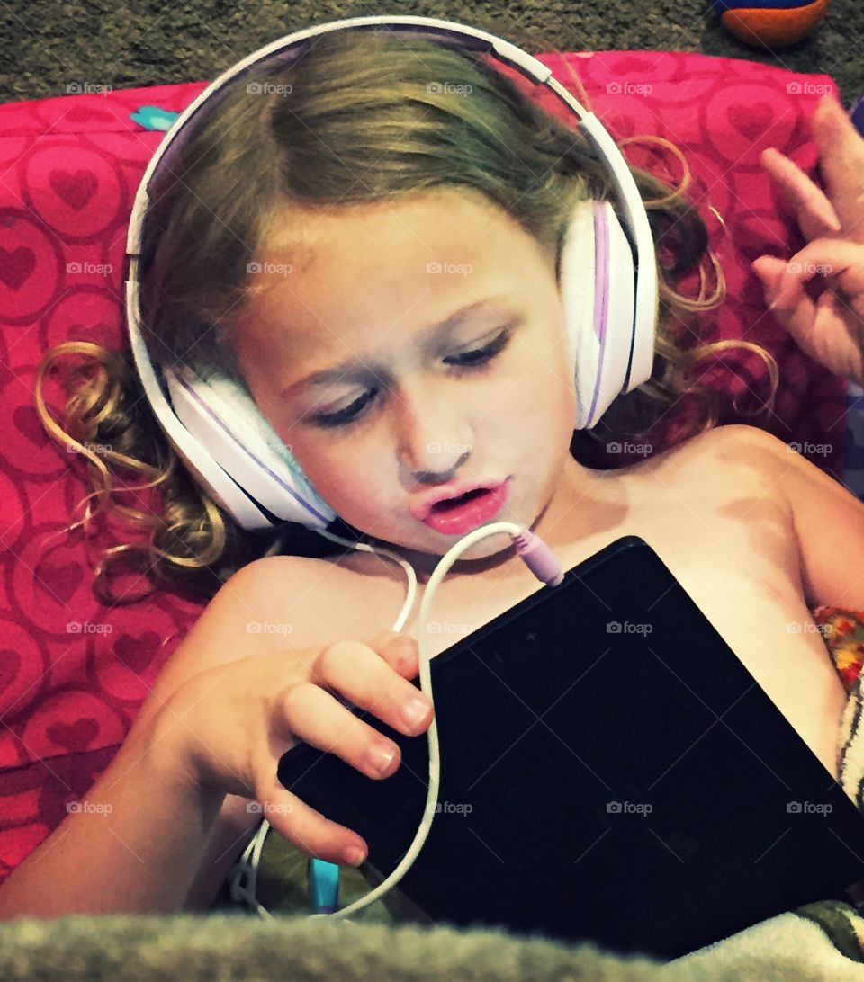 Young girl lying on the bed with headphones and tablet