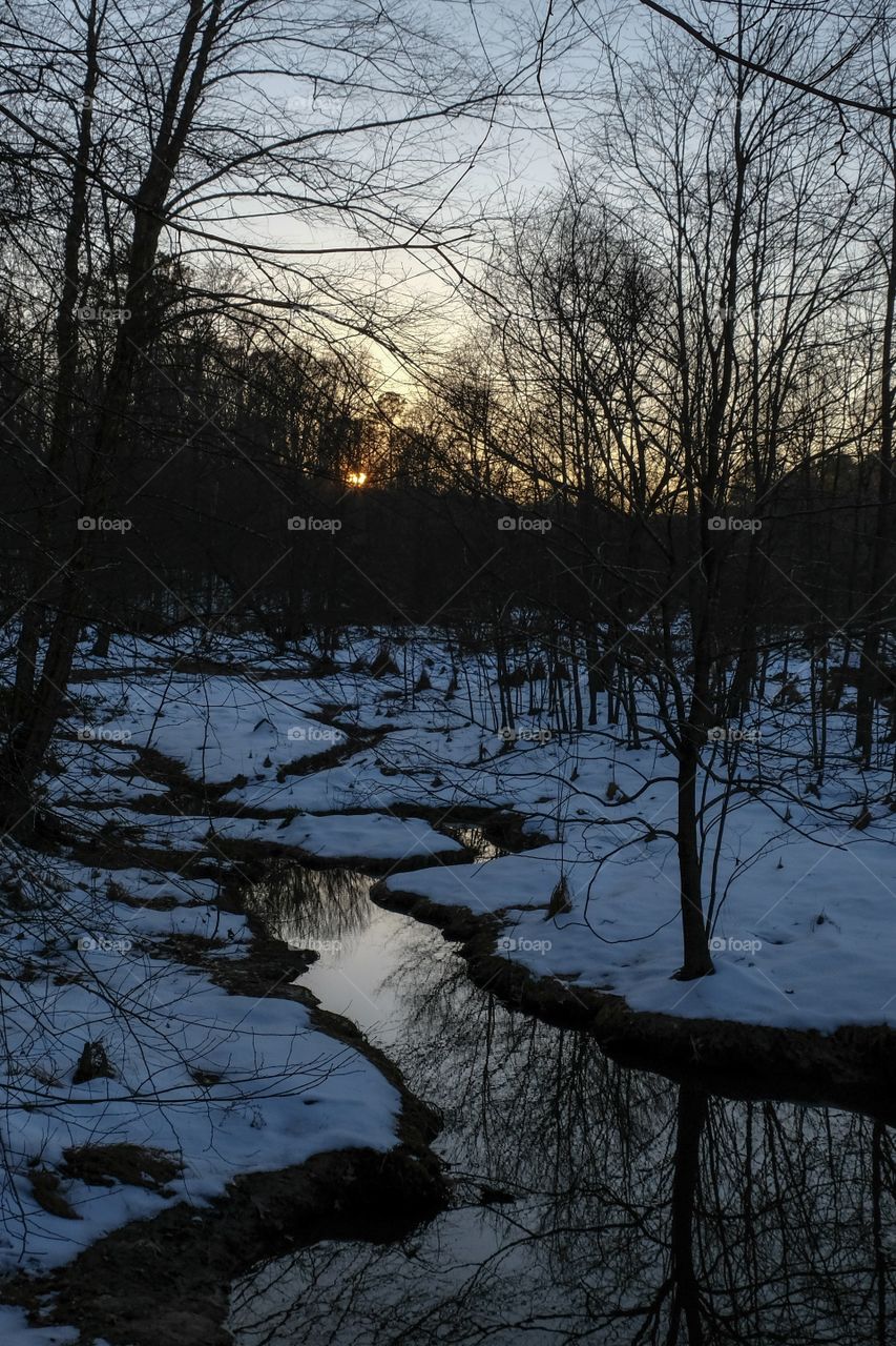 The sun takes one last peek at the meandering stream running through the snow covered landscape at Yates Mill County Park in Raleigh North Carolina.