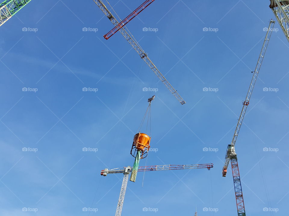 Cranes at a construction site lifting concrete with blue sky in the background