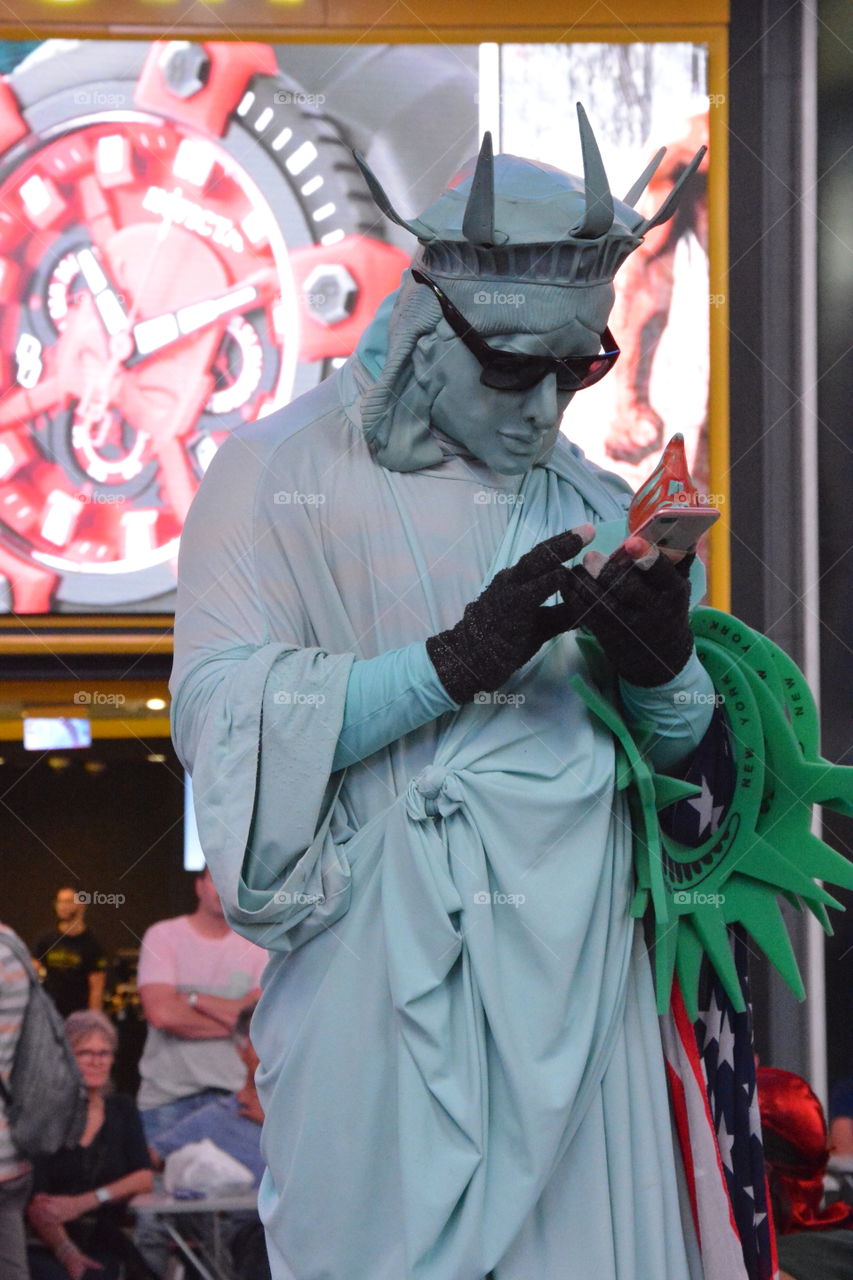 Person in a Statue of Liberty costume in NYC Times Square takes a work break to text on phone