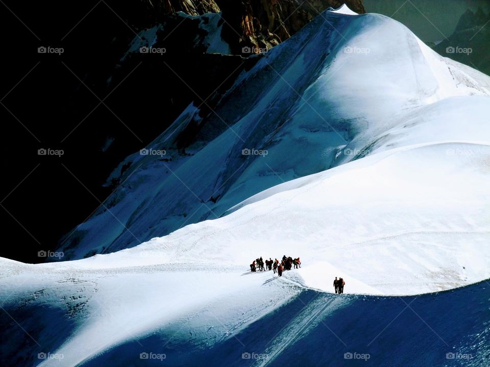 A group of climbers whose figures are outlined in the sunlight on on a snowy ridge below Mont Blanc with sunlight and shadows