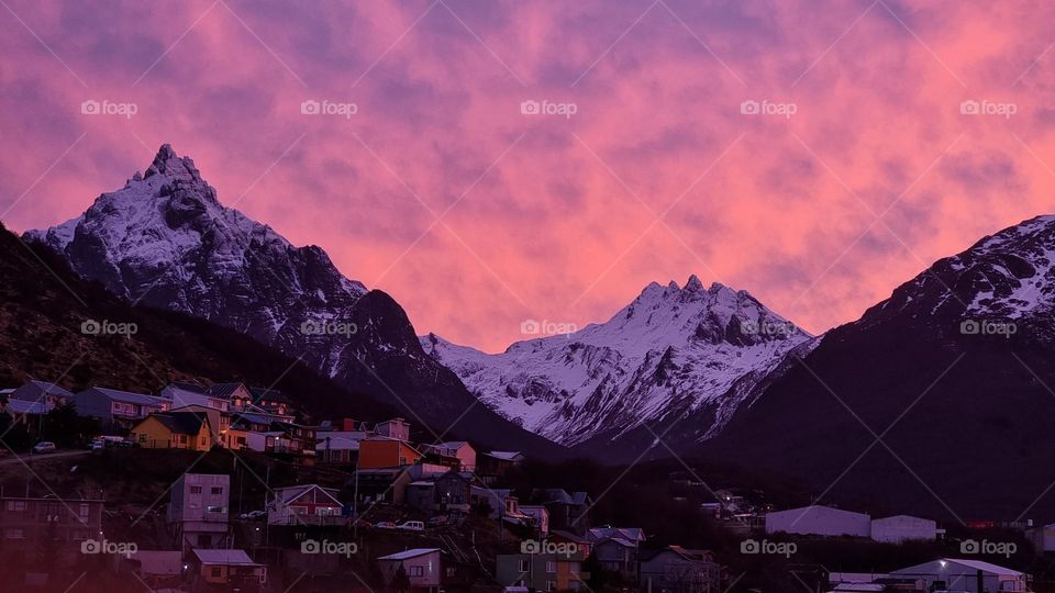 pink cloudy sunset over the snowy mountains and some houses.