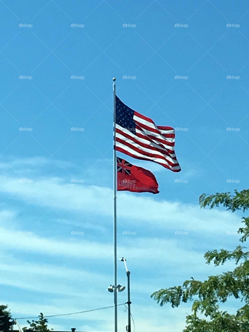 Roadside American Flag 🇺🇸 on flagpole flying above the Confederate Flag, blue sky on windy day with clouds.