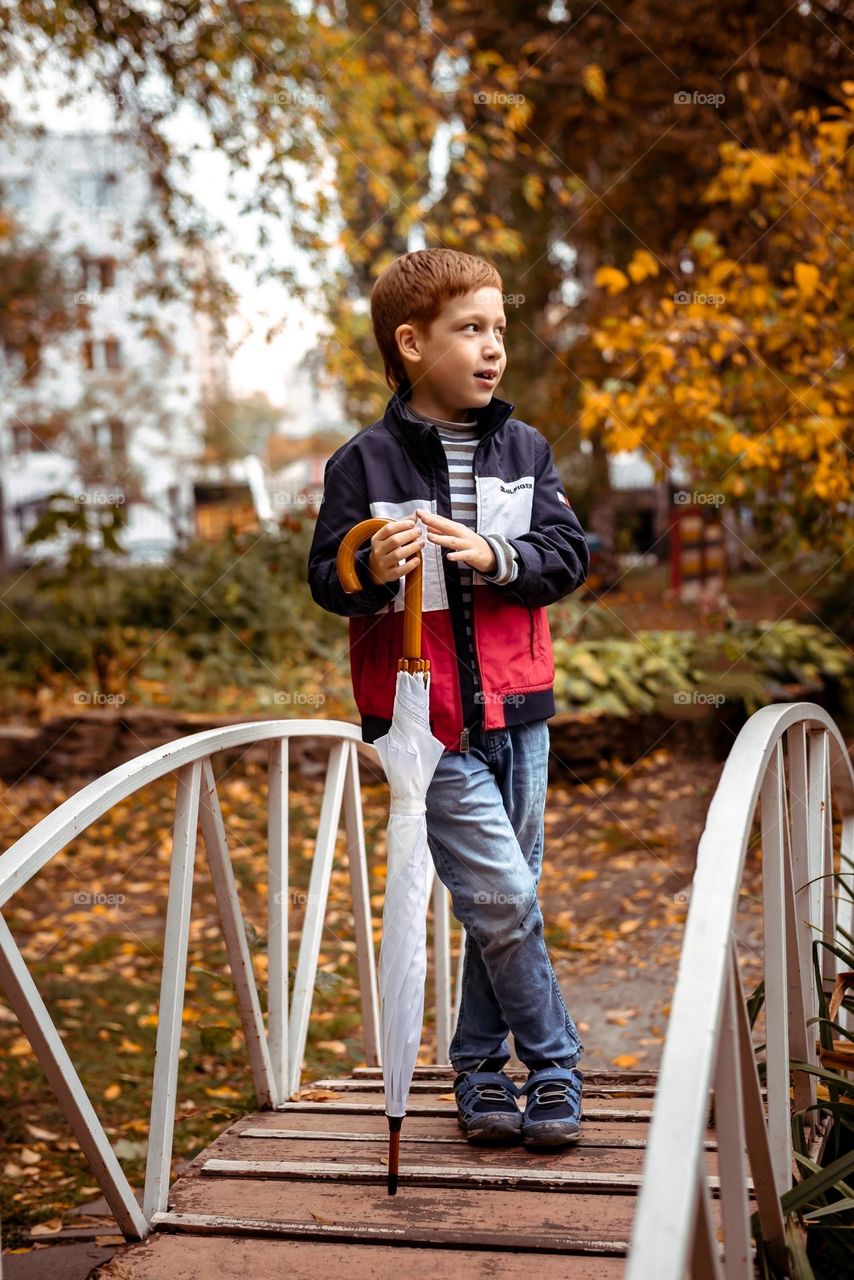 Child boy walking in the autumn park stands on the bridge with an umbrella